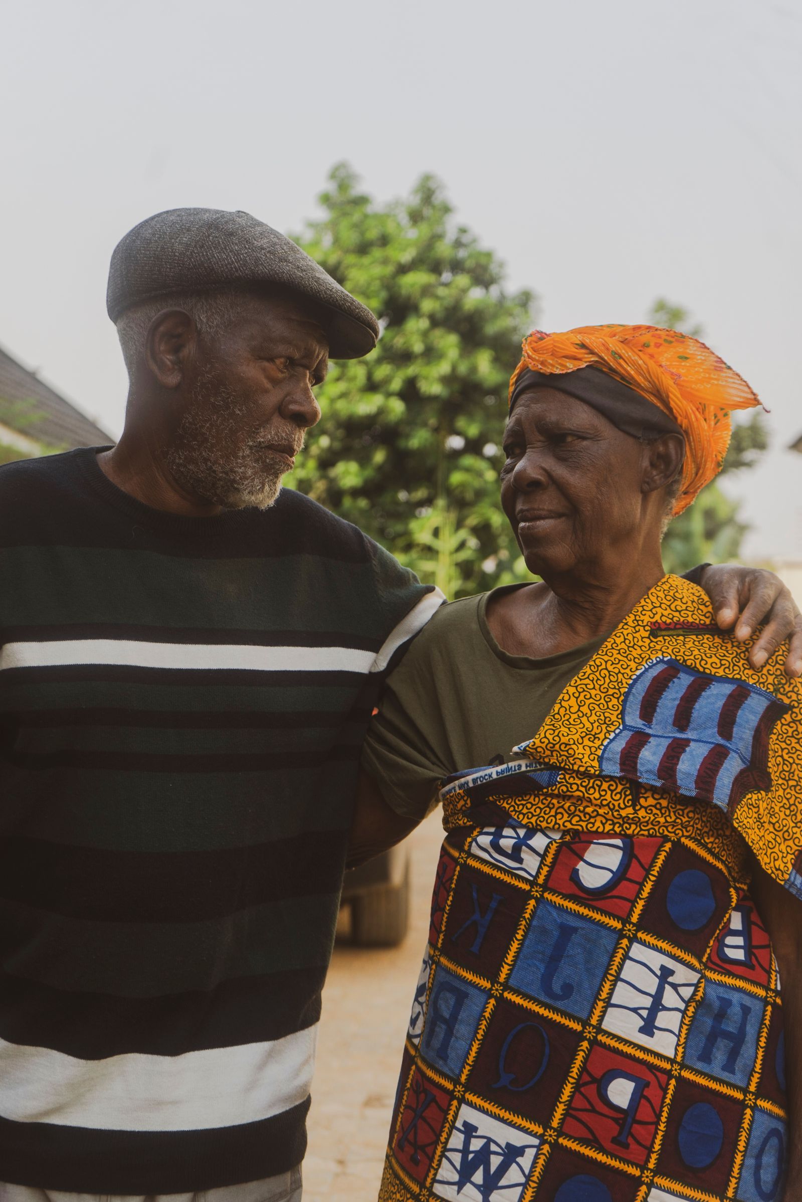An elderly couple standing arm in arm outdoors.