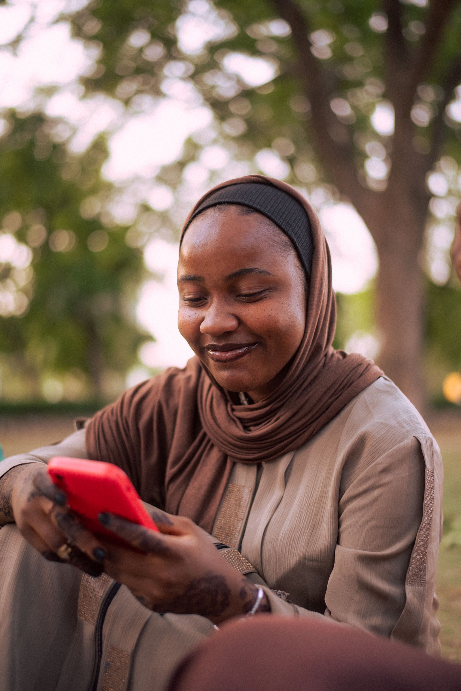 A smiling woman in a hijab checking her phone outdoors.