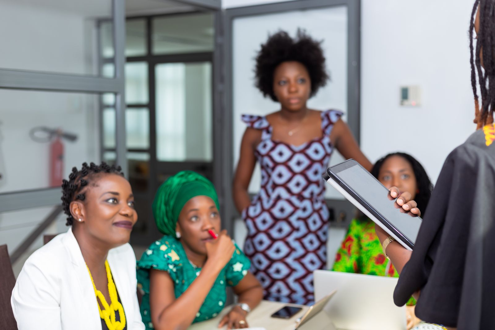A team of women in a meeting, one presenting from a tablet.